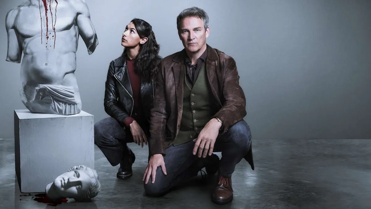 Stephen Moyer as DI Mick Palmer and Nina Singh as DC Shazia Malik pose bending down to investigate a broken statue in a museum