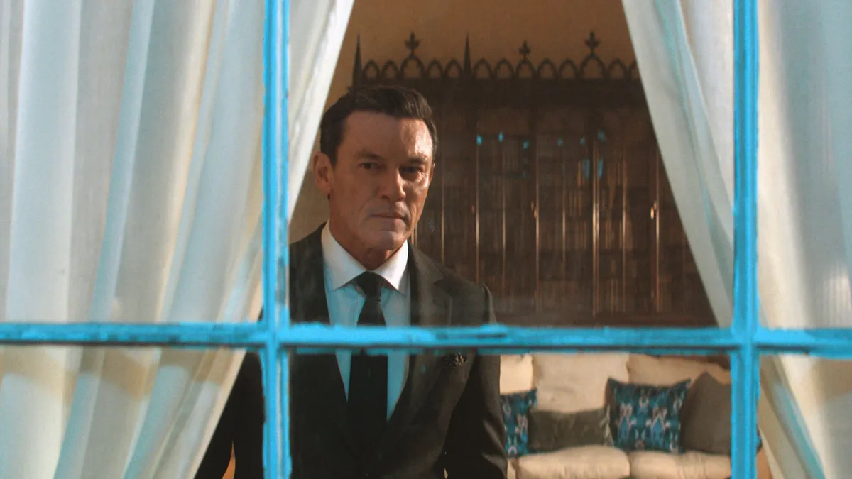Luke Evans as Martin Gilmour, pictured through a window in a house