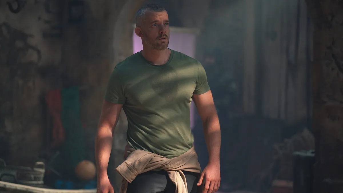 Russell Tovey as Barclay: A man in a t-shirt stands in the shadows looking up at something off screen