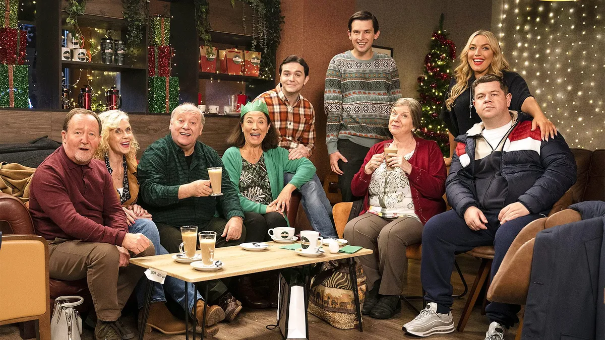The cast of Two Doors Down sat on sofas in a living room